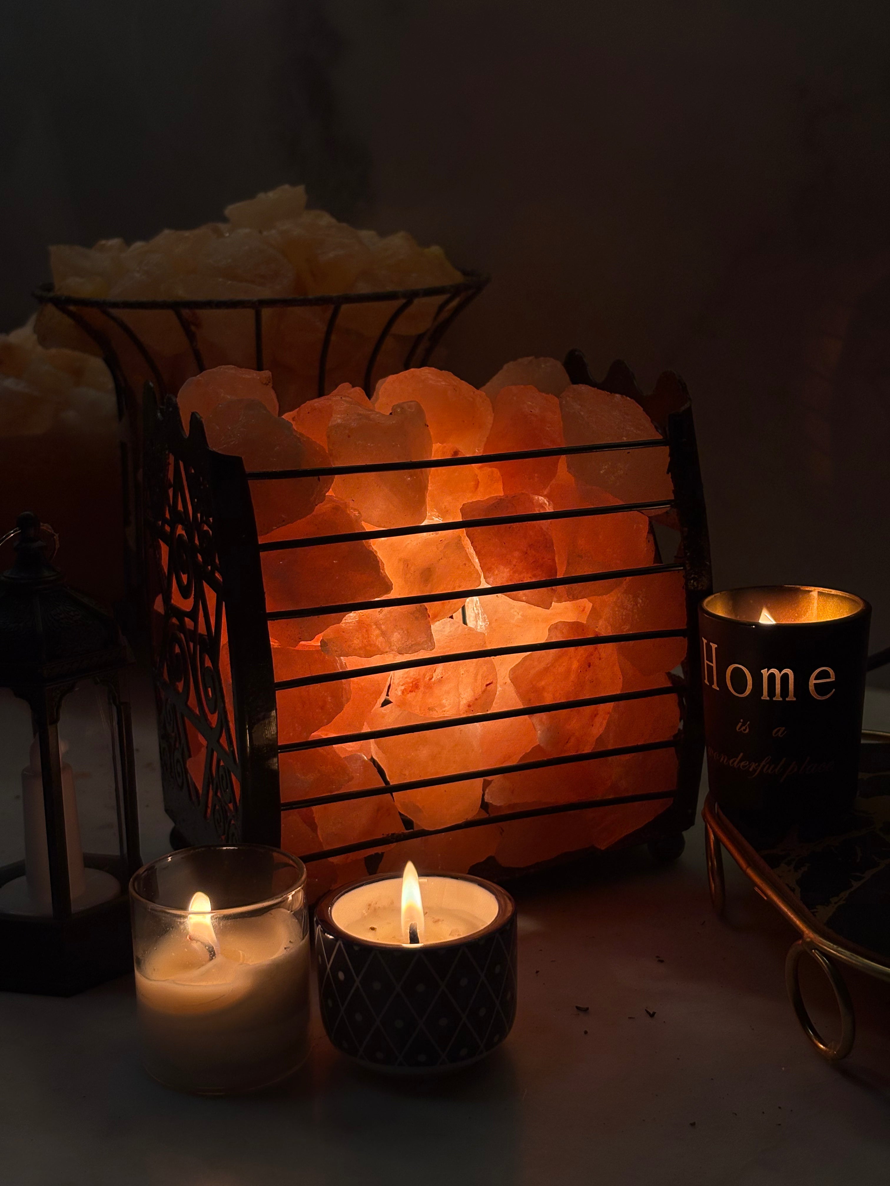 Himalayan salt lamp emitting a warm glow with candles and a decorative item in the foreground. Main image